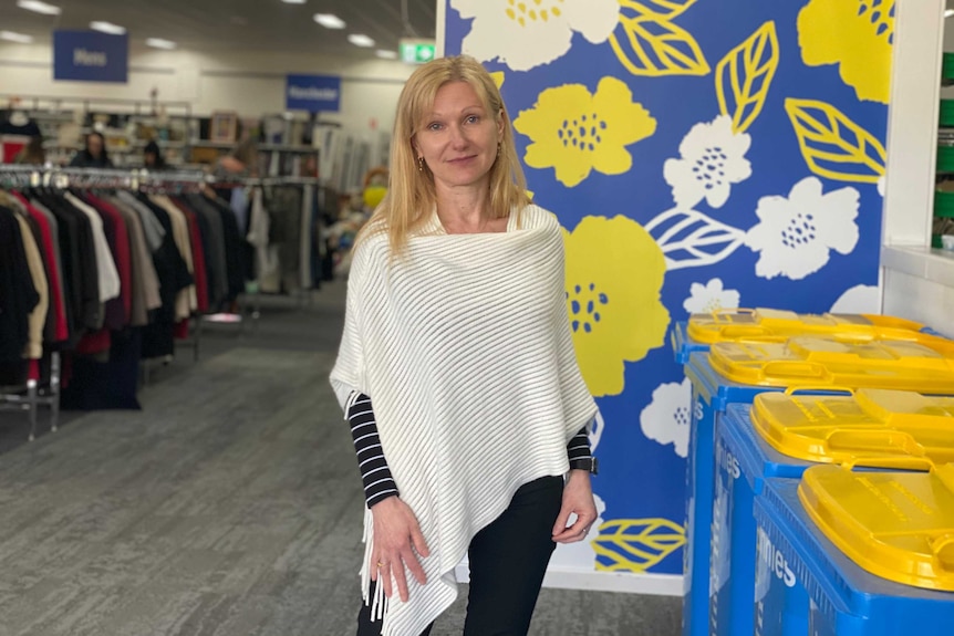 A woman stands in front of donation bins inside a charity shop.