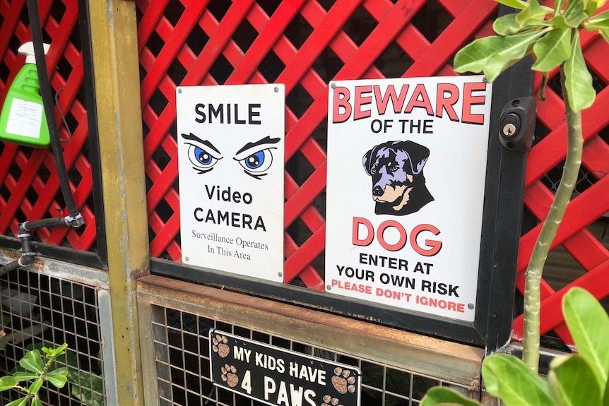 A photo of signs on the side of a house warning people about dogs and surveillance cameras.