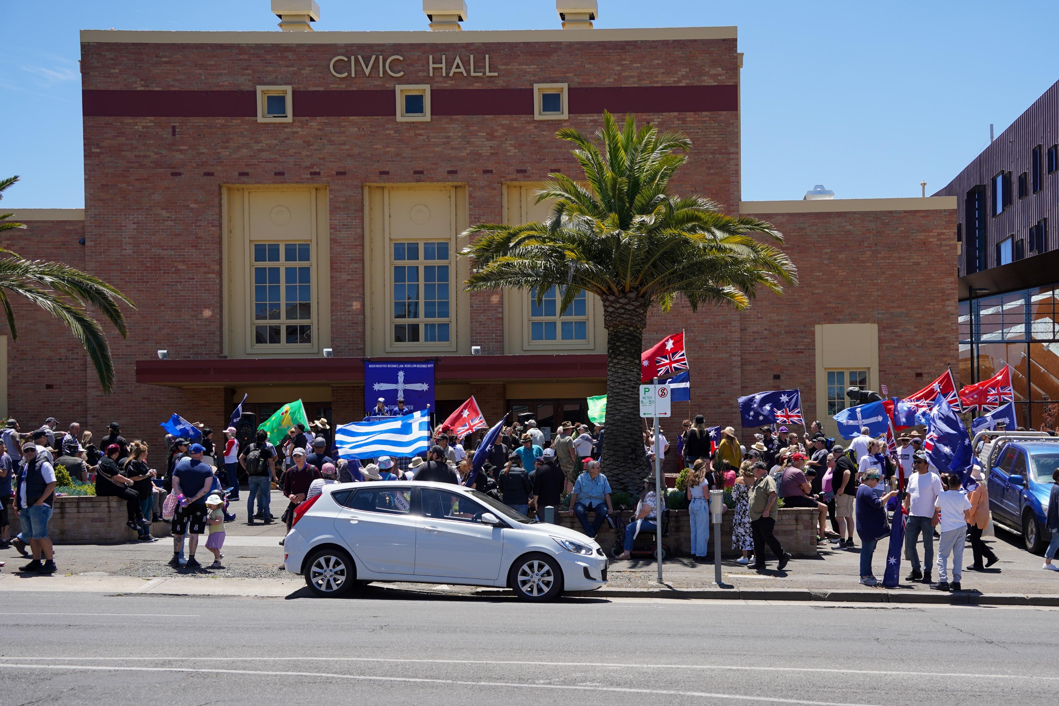 Group of people waving flags in front of building on sunny day.