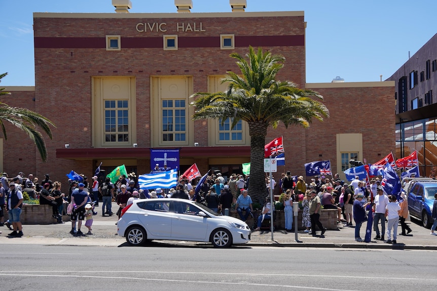Group of people waving flags in front of building on sunny day.