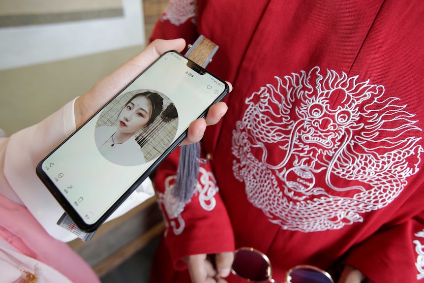 A woman holds up a smartphone against a bright red traditional red Chinese coat.
