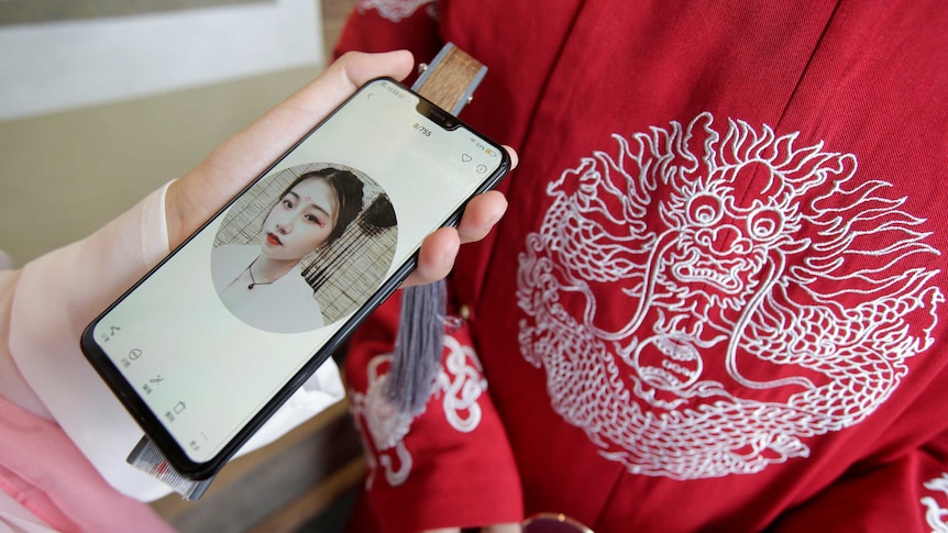 A woman holds up a smartphone against a bright red traditional red Chinese coat.