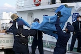 Four men in coast guard uniforms and masks help carry a bag 