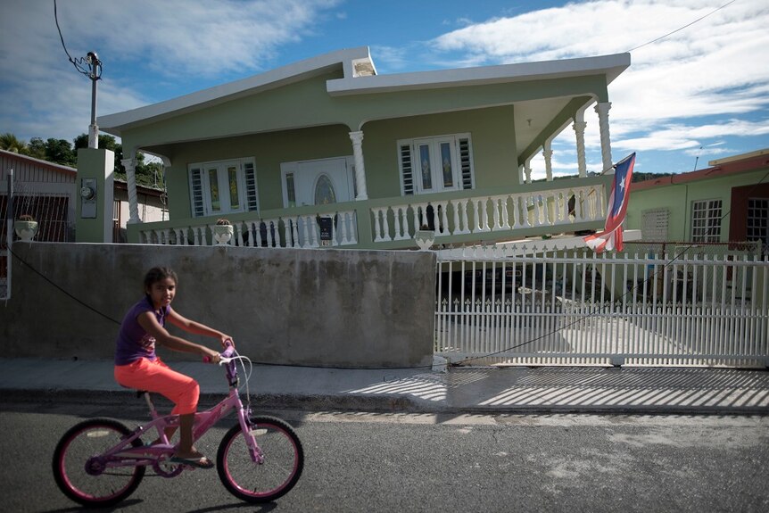 A girl cycles past a house in Puerto Rico where an earthquake hit.