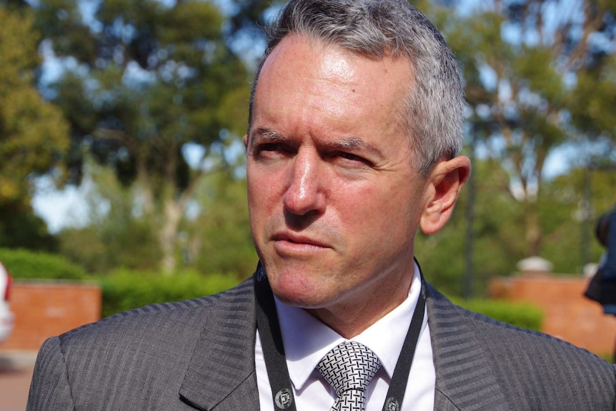 Terry Redman outside speaking to reporters wearing a grey suit, white shirt and black and white tie.