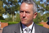 Terry Redman outside speaking to reporters wearing a grey suit, white shirt and black and white tie.