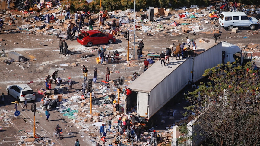 An aerial shot of a street corner with refuse everywhere and people looting a semi-trailer. 