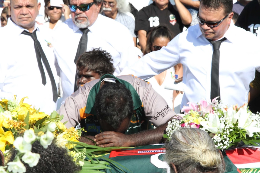 A man rests his head on the coffin at the funeral of Jack Long in Darwin