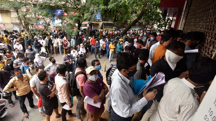 A large crowd of people queue untidily outside a building. 