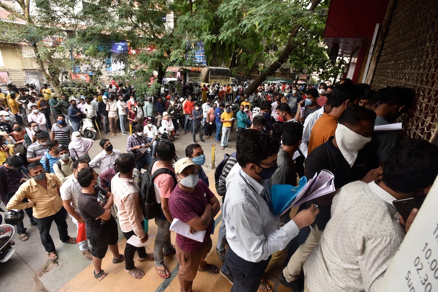 A large crowd of people queue untidily outside a building. 