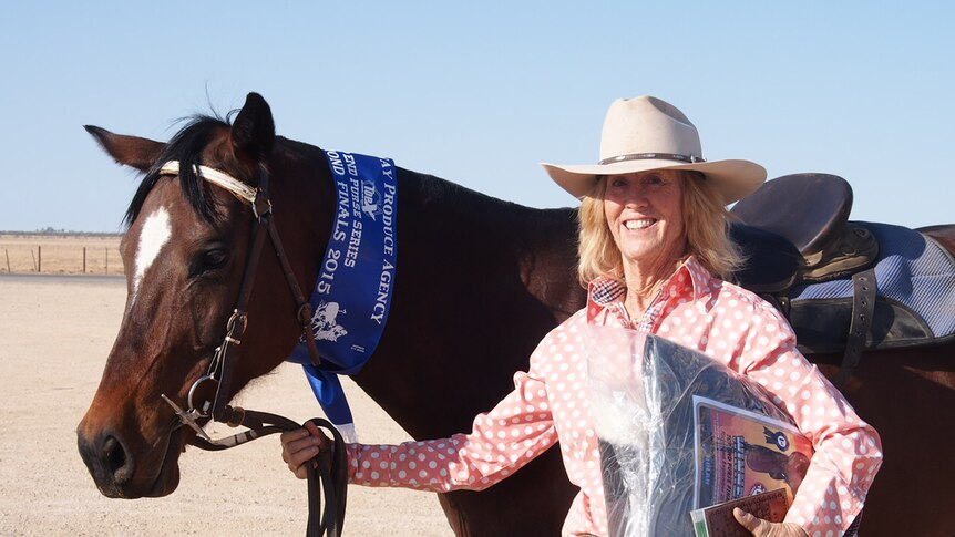 Dallas Daley, dressed in a pink short and wide-brim hat, holds her horse after winning a competition.