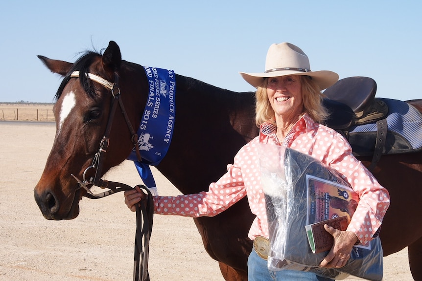 Dallas Daley, dressed in a pink short and wide-brim hat, holds her horse after winning a competition.
