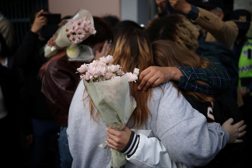 Young women holding bunches of flowers hug each other