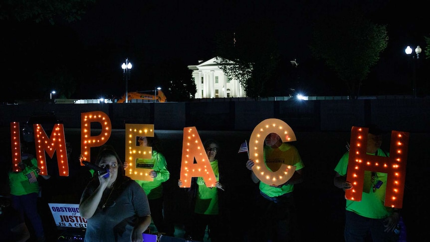 Protesters holding up letters spelling the word impeach standing outside the White House at night.