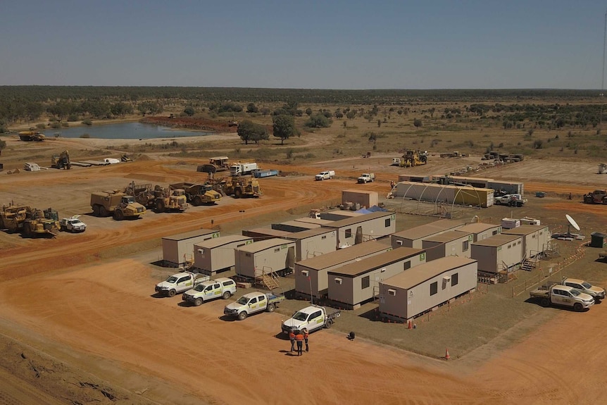 Dongas surrounded by dirt, with a dam in the background.