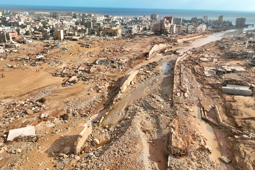 An aerial photo of a coastal historic city with many destroyed buildings and a wide divide in the middle cleared by a flood