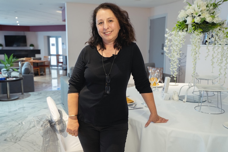 Antonia dressed in black learning on a table in a hotel dining room.