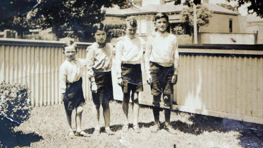 A black and white photo shows four young boys standing in the front yard