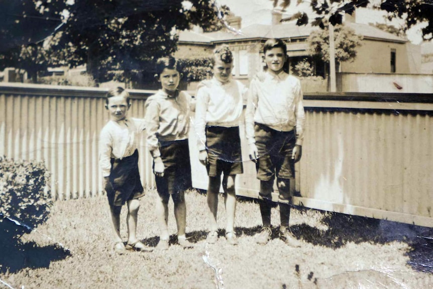 A black and white photo shows four young boys standing in the front yard