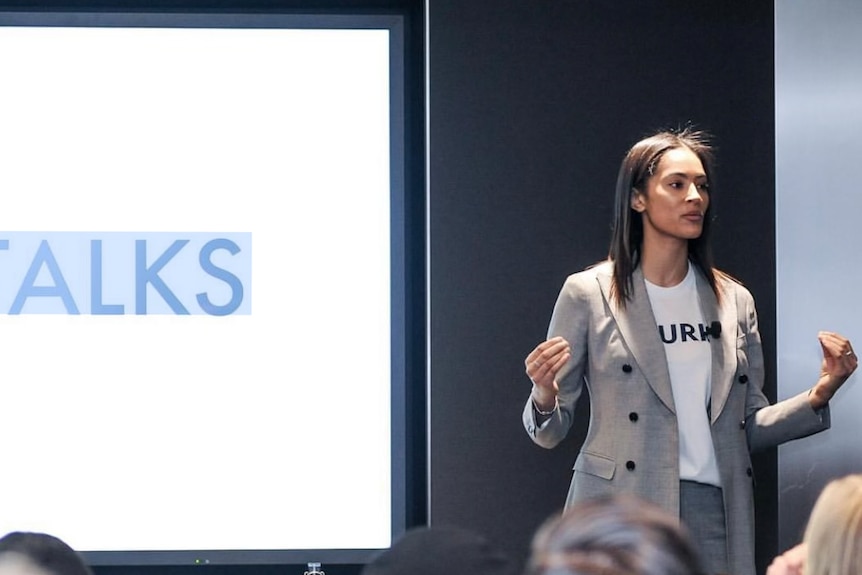 A woman give a lecture while standing in front of a projected screen.