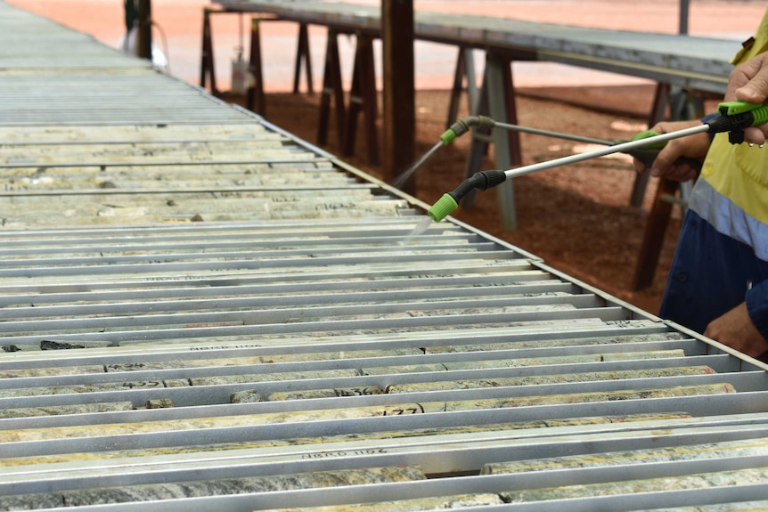 Long round stone samples lined up in a long tray being sprayed with water