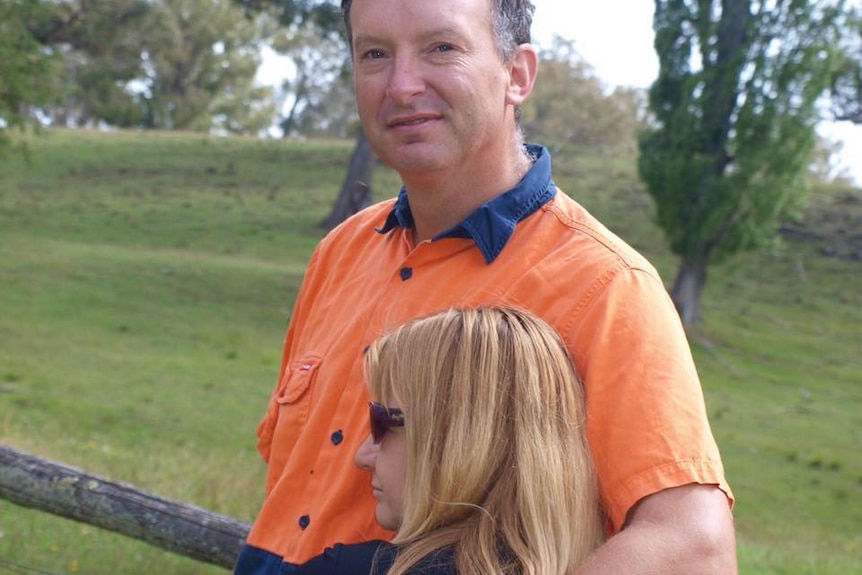 Man in a farm setting smiles as he holds a woman against him.