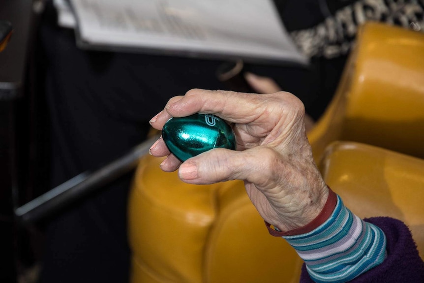 An elderly woman's hand holding a colourful egg shaker