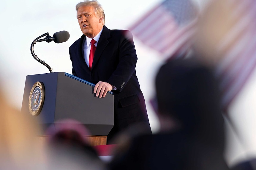 Donald Trump speaks at a podium as US flags fly behind him