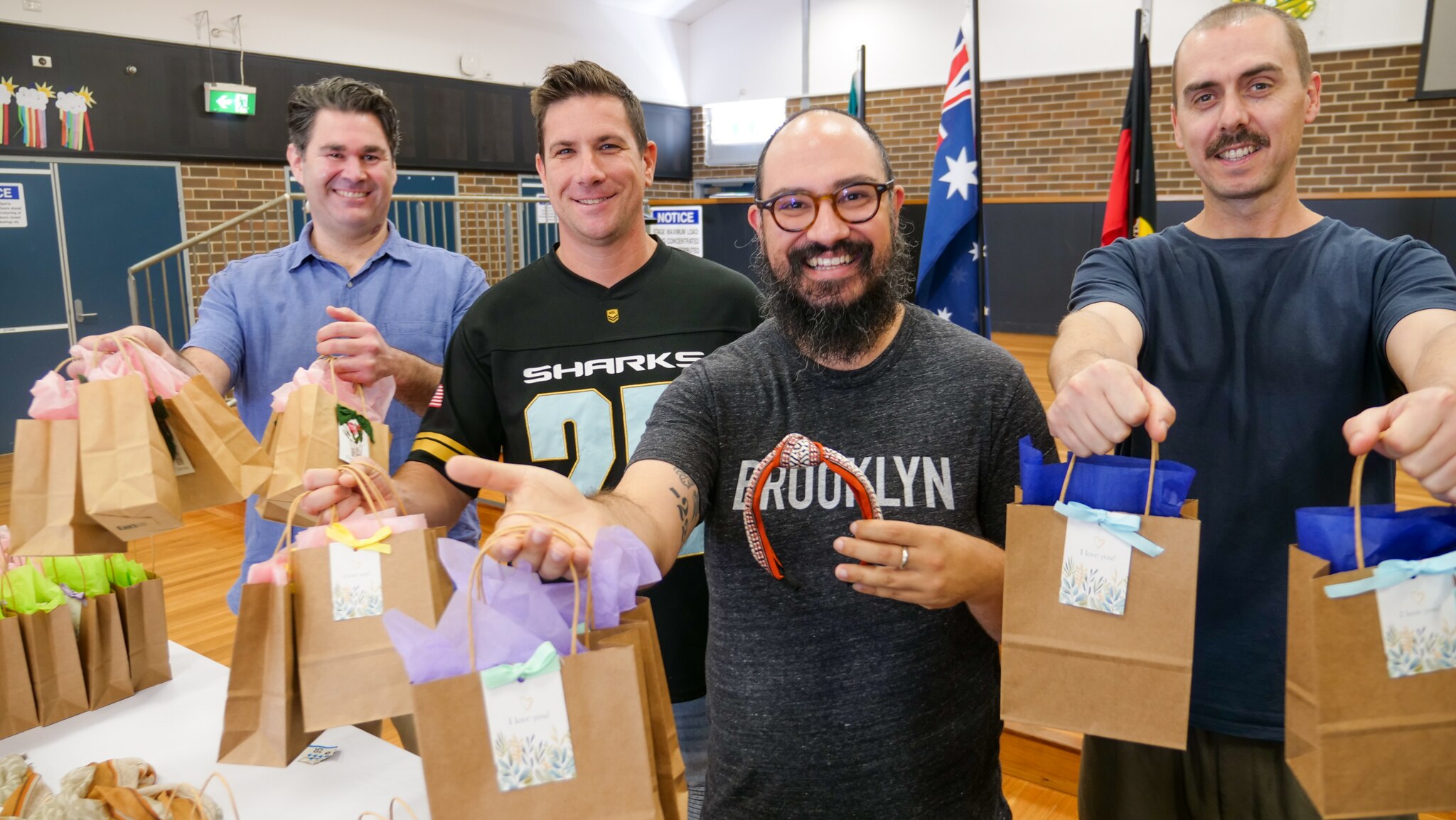 Four men hold wrapped gifts in a school hall. 
