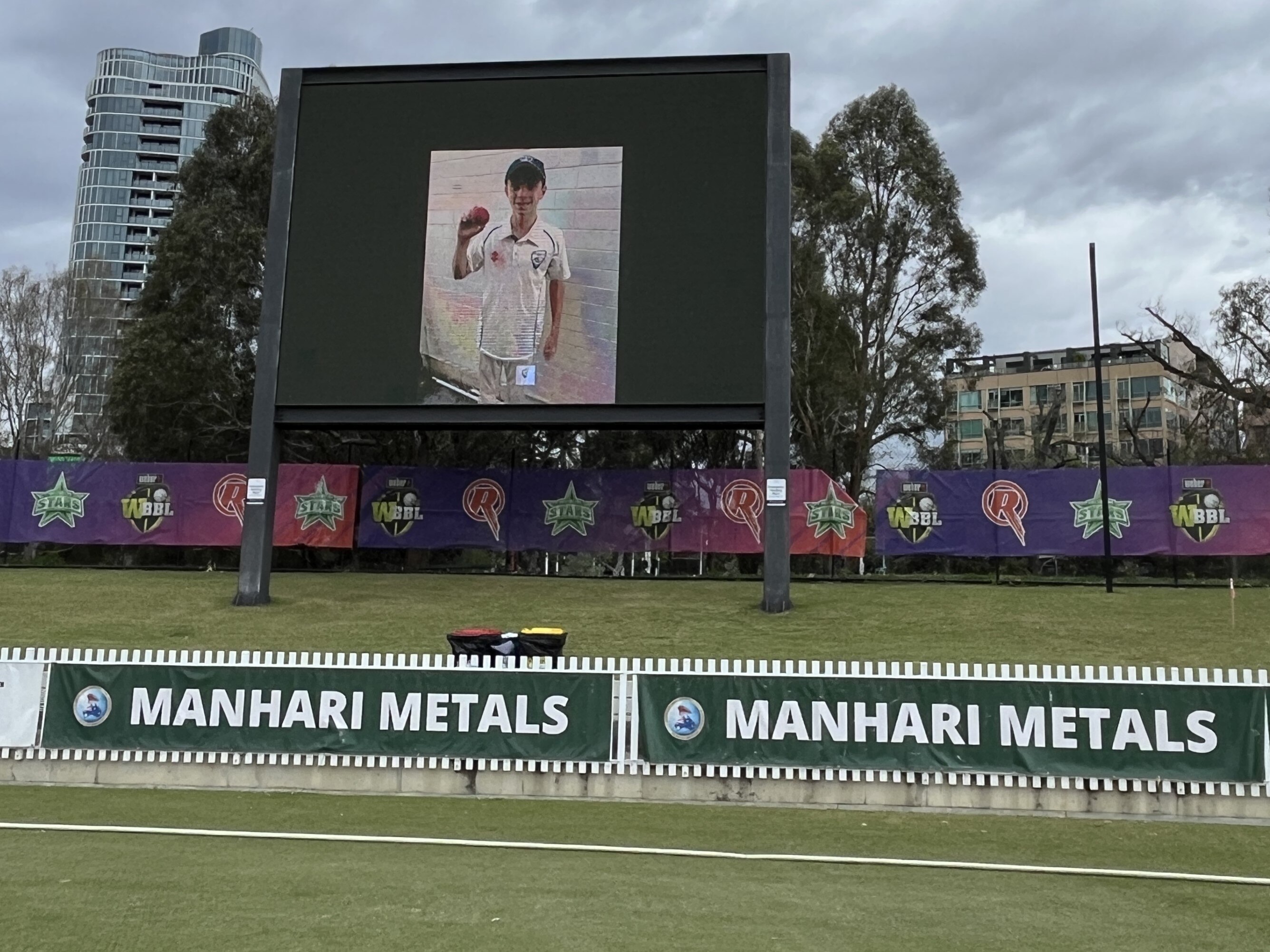 Ben Austin's photo on a screen at a cricket ground