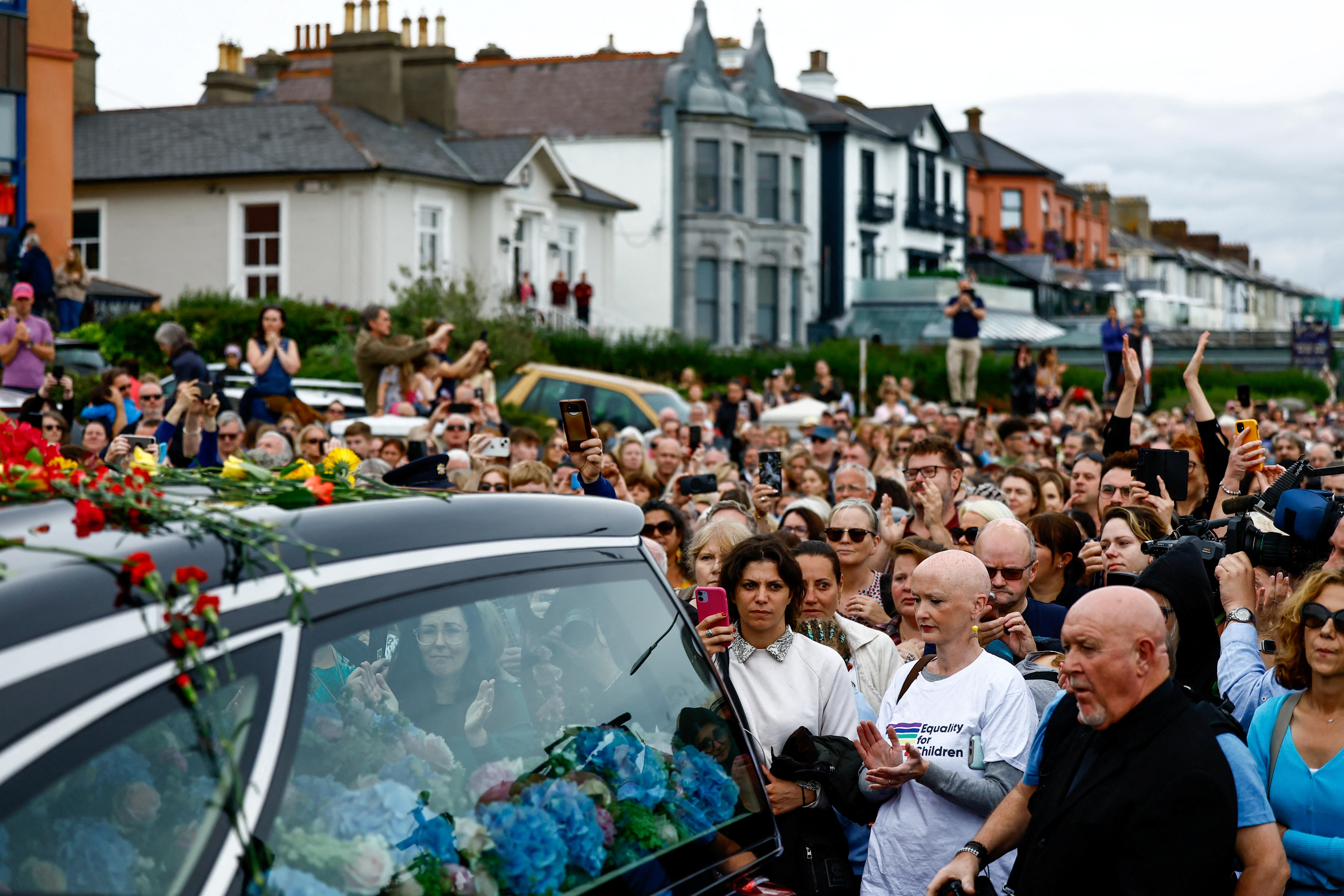 A large group gathered around a hearse. 