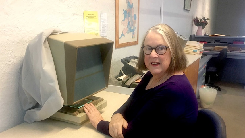 Genealogist Sue McBeth sits at a desk with an archives machine.