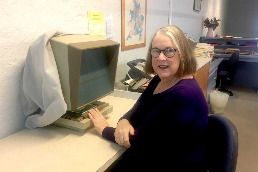 Genealogist Sue McBeth sits at a desk with an archives machine.