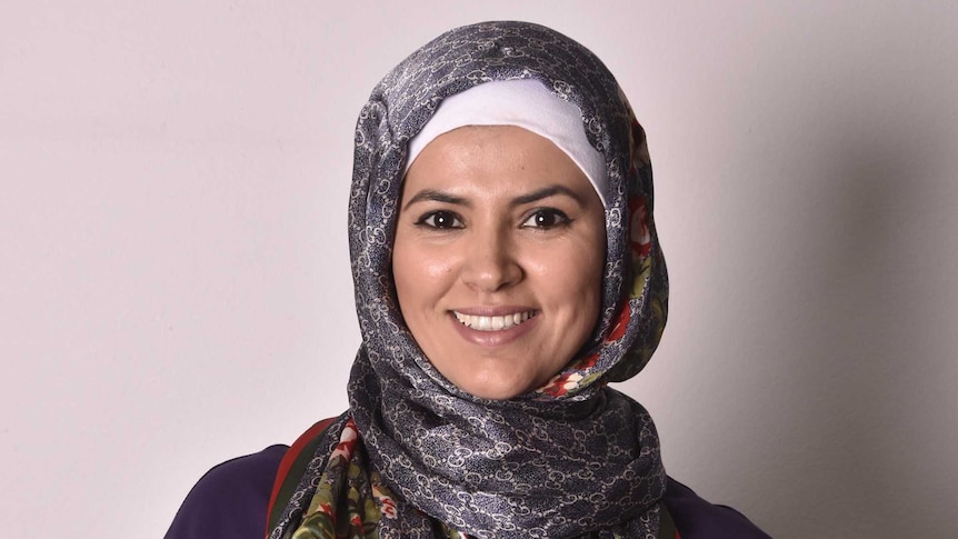 Young Moroccan lady smiles at the camera. She is wearing a patterned headscarf and dark purple blouse