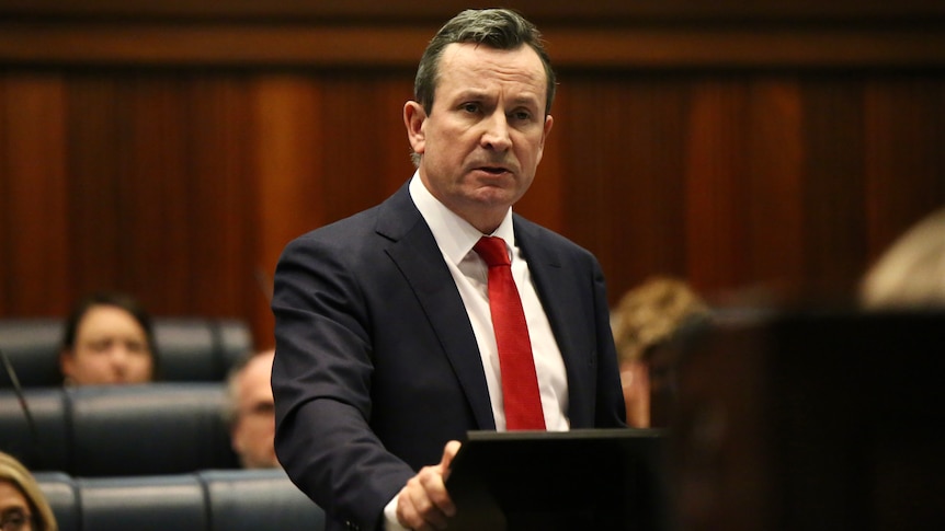 A mid-shot of Mark McGowan at a lectern wearing a red tie.