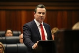 A mid-shot of Mark McGowan at a lectern wearing a red tie.
