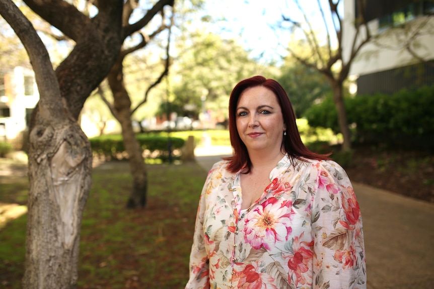 A woman in a floral shirt stands in a park.