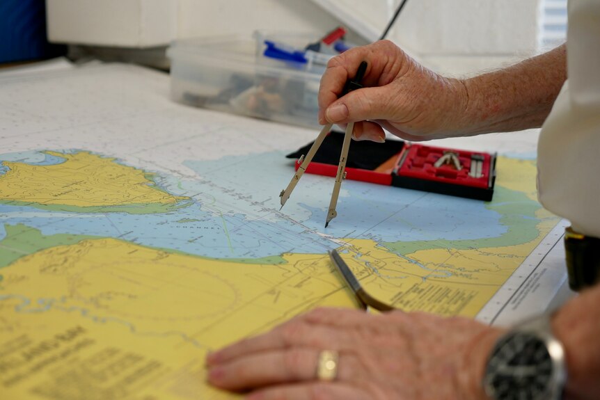 A colorful chart off the Queensland coast. A hand is holding a compass to the page.