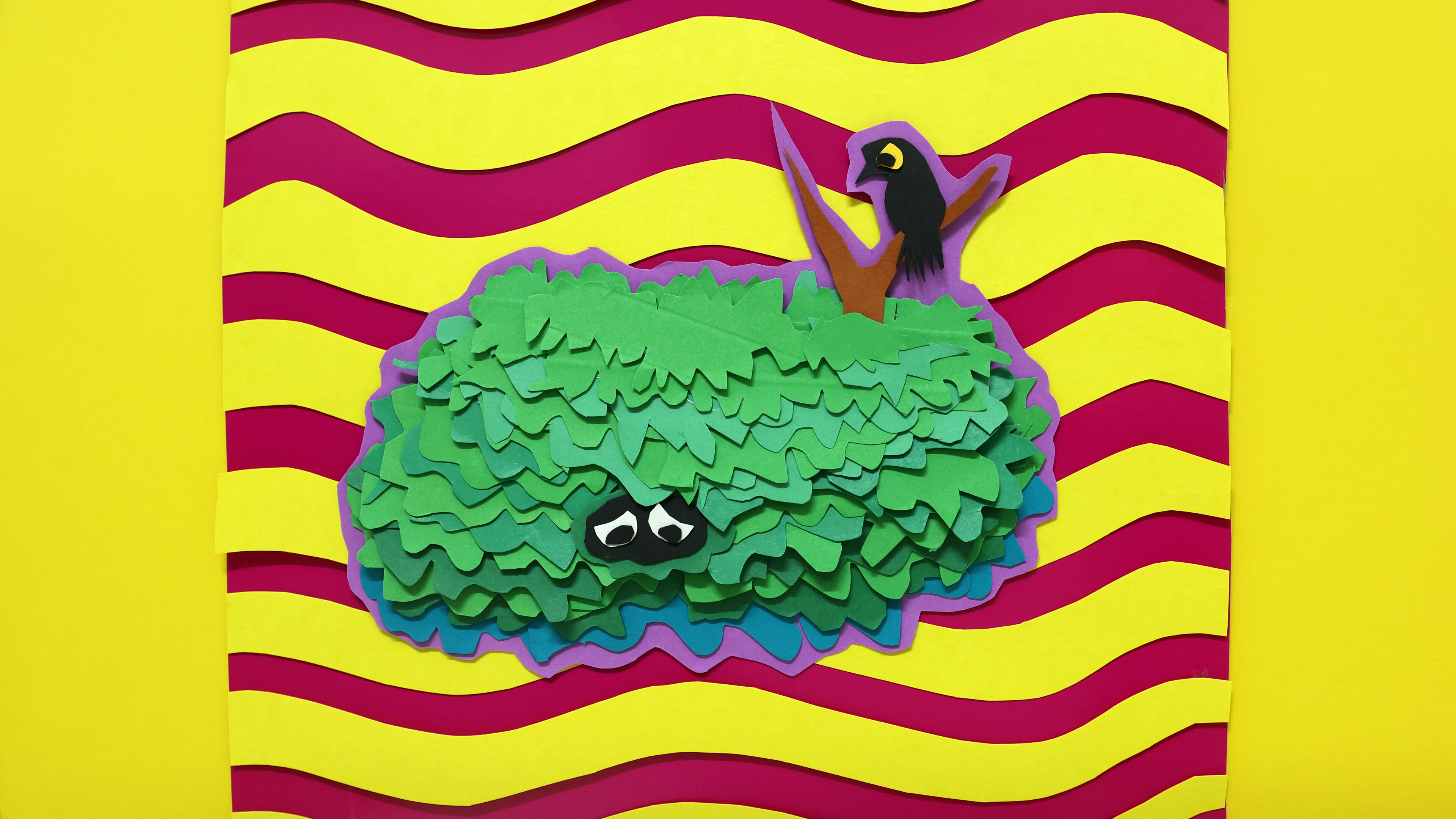 An artworks shows a green bush with eyes in the middle and a branch poking out the top with a black bird perched on it.