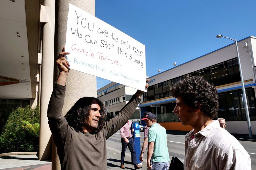 Photograph of a man holding a sign talking to another man