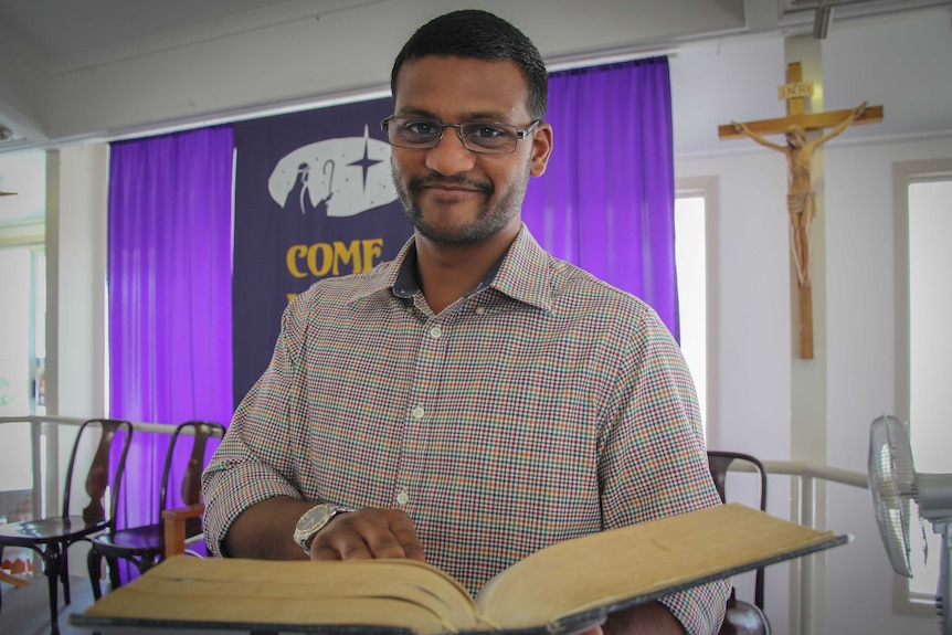 25-year-old Ashwin Acharya holds a bible as he looks at the camera.