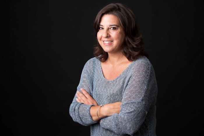 A middle-aged Italian Australian woman stands with her arms folded, smiling, wearing a grey blouse.