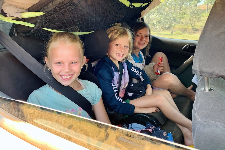 Three children sit across the back seat of a four-wheel drive vehicle.