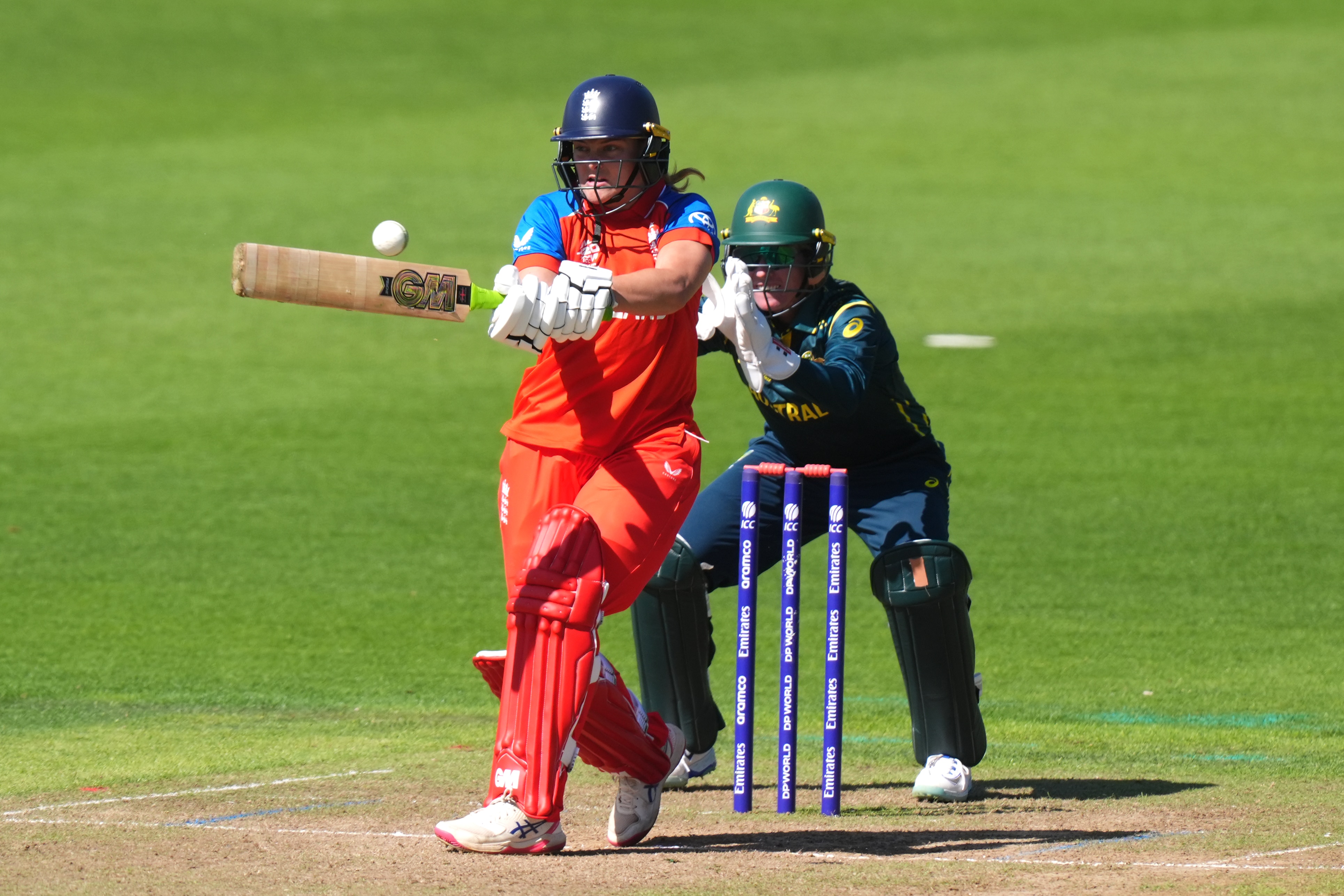 Dani Gibson swings her bat to hit the ball. Behind her, the Australian wicketkeeper has her hands out, ready.