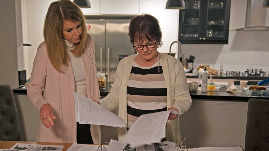 Two women stand at a kitchen table going through paperwork