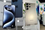 A composite of two images: The front of an iPhone 15 Pro on a stand, and the back of a Samsung Galaxy S24 Ultra on a stand.