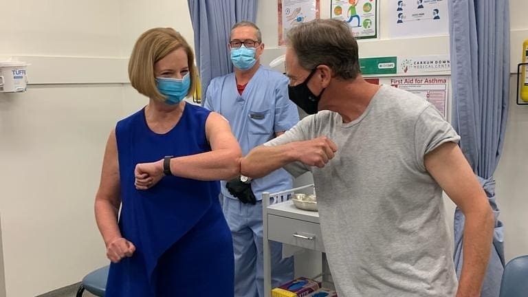 Greg Hunt and Julia Gillard bump elbows while wearing masks.
