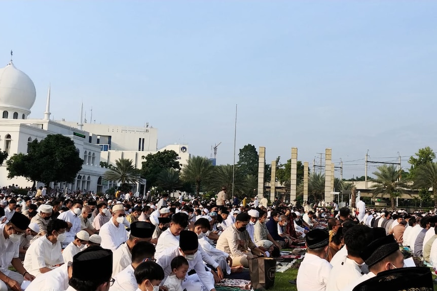 People sitting down in shaft in a fielld for ied pray with a mosque at the background