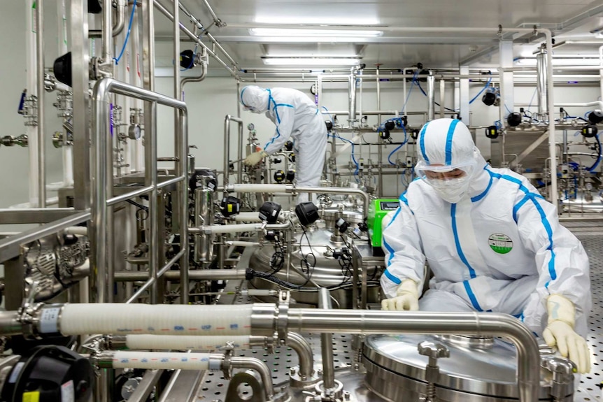 Workers in full protective gear tend to shiny metal apparatuses