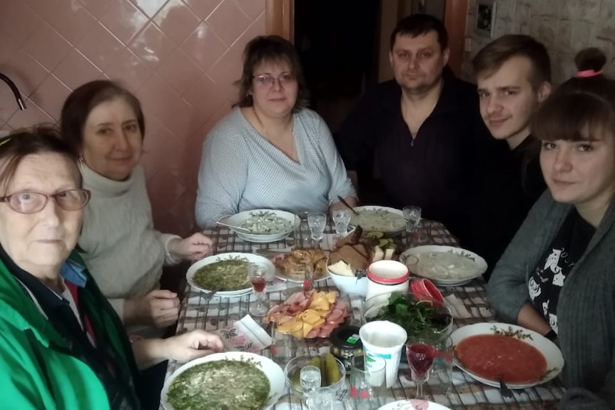 A Ukrainian family sits around a table in their home.  